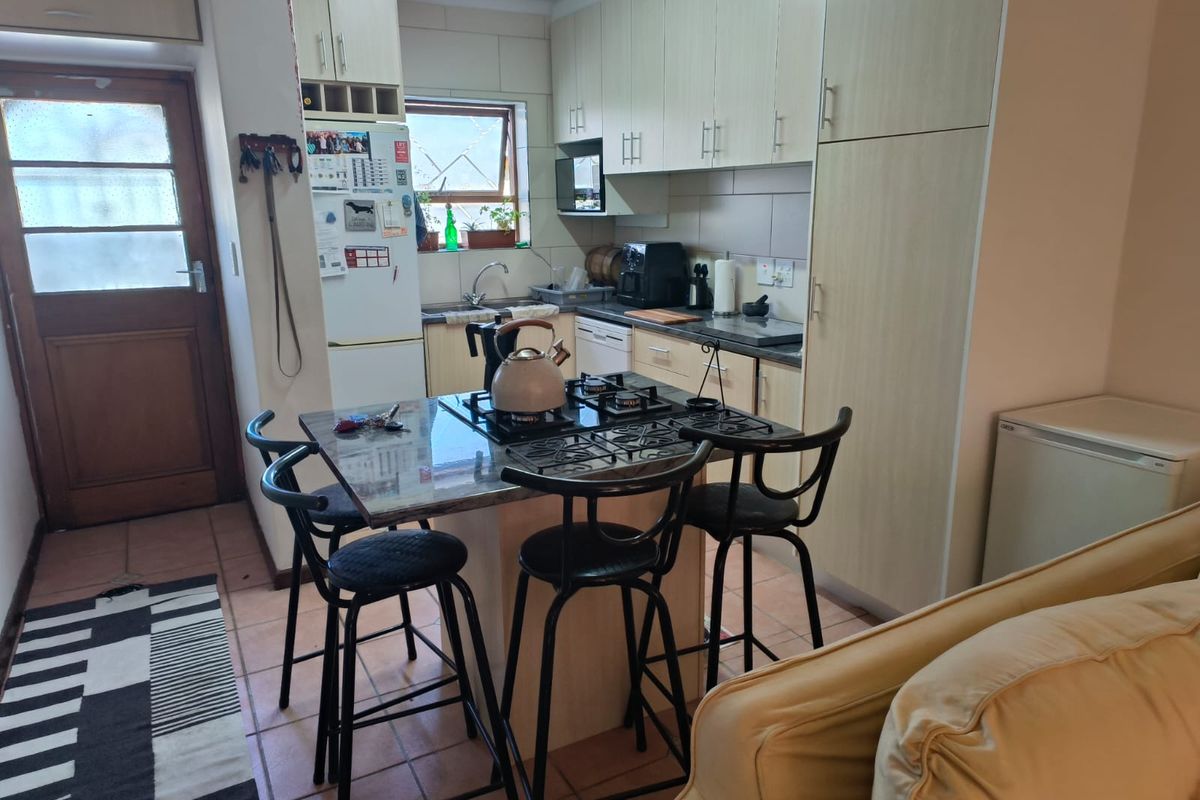 A functional kitchen featuring light-toned built-in cabinetry, a central island with a gas hob, tiled flooring, and a tiled backsplash.