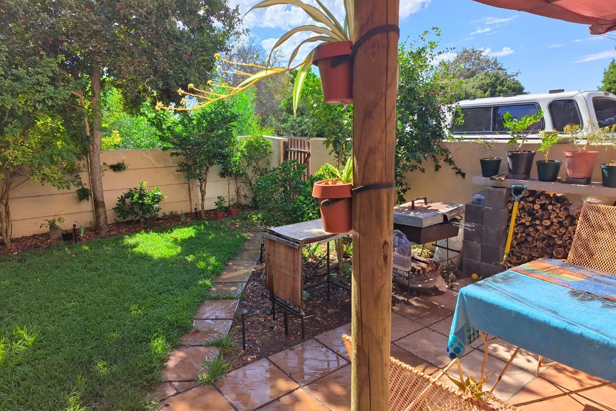 A private rear garden featuring a paved patio area with a built-in braai, timber support post, and established lawn.