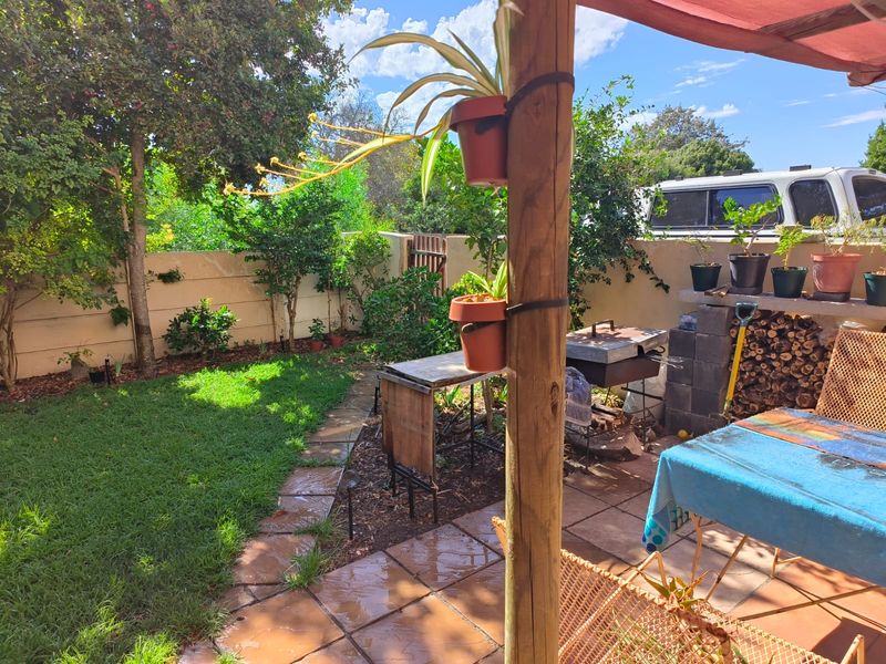 A private rear garden featuring a paved patio area with a built-in braai, timber support post, and established lawn.