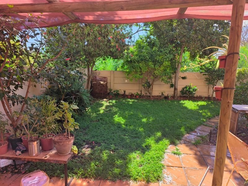A private garden featuring a lawn, paved patio area, and a timber pergola structure, enclosed by a precast concrete boundary wall.