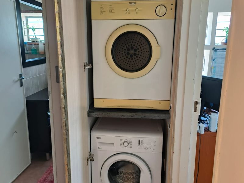 A compact built-in laundry cupboard designed for stacked appliances, featuring integrated shelving within a dedicated utility space.