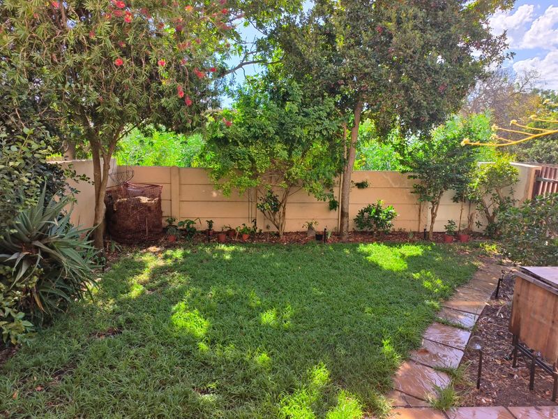 A private garden area featuring a well-maintained lawn, established trees, and a stone paved pathway enclosed by a precast concrete boundary wall.