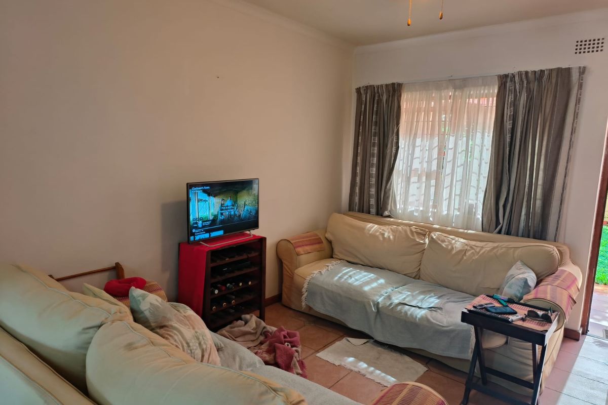 A functional living room featuring tiled flooring and a ceiling fan, with natural light entering through a window with curtain tracks.