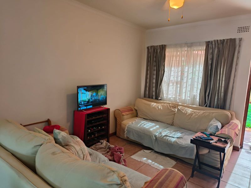 A functional living room featuring tiled flooring and a ceiling fan, with natural light entering through a window with curtain tracks.
