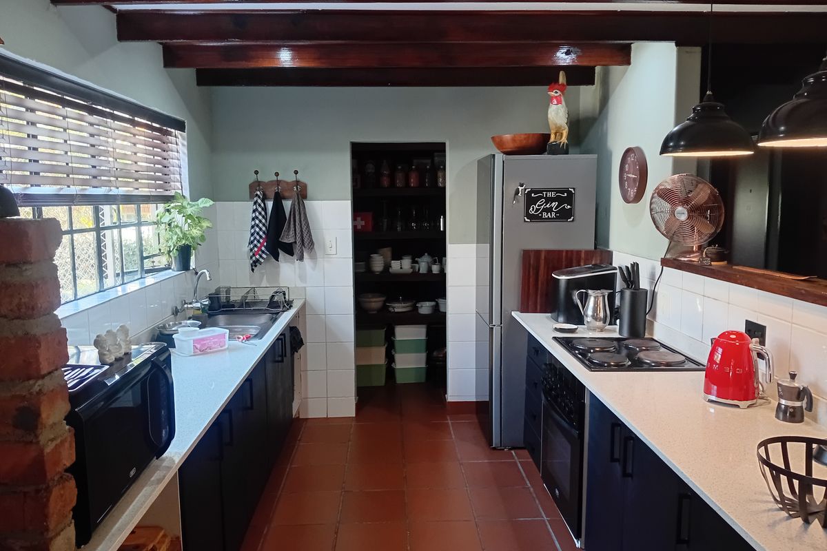 A functional kitchen featuring exposed timber ceiling beams, dark cabinetry, stone countertops, and a convenient walk-in pantry with terracotta flooring.