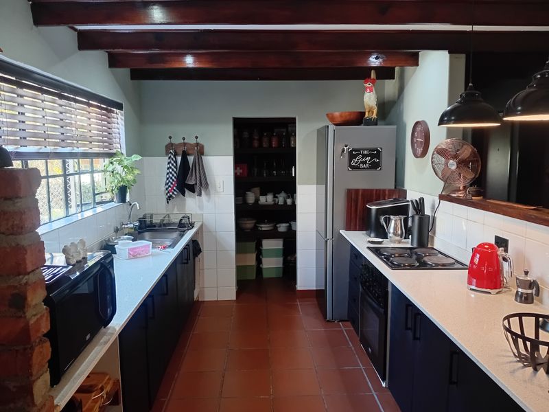 A functional kitchen featuring exposed timber ceiling beams, dark cabinetry, stone countertops, and a convenient walk-in pantry with terracotta flooring.