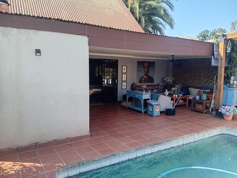 Covered outdoor patio area featuring tiled flooring, exposed brickwork, and a ceiling fan, overlooking a swimming pool.