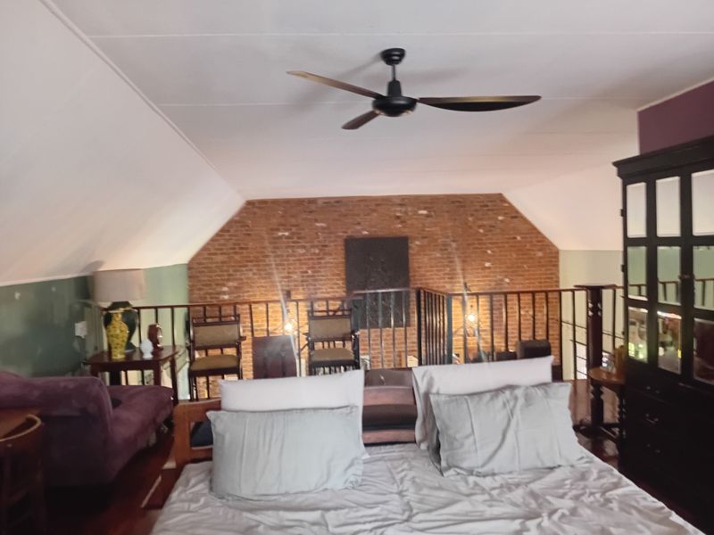 A spacious bedroom featuring a unique mezzanine level with exposed brickwork, hardwood flooring, and a ceiling fan, overlooking the lower living area.
