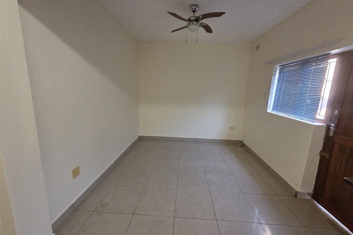 An empty bedroom featuring neutral tiled flooring, a ceiling fan, and a window with venetian blinds.