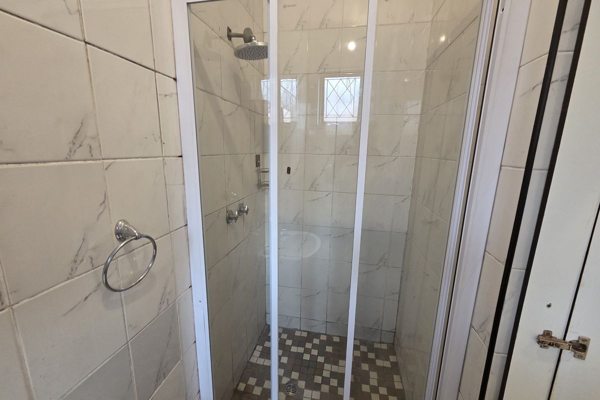 A clean bathroom shower enclosure featuring marble-look wall tiles, a mosaic tiled floor, and a modern shower head fixture.