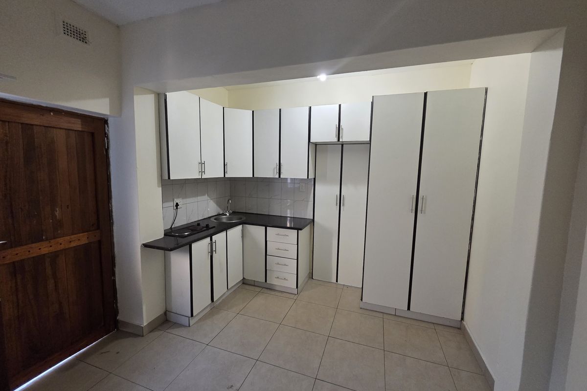 A clean, functional kitchen featuring white built-in cabinetry, dark countertops, tiled flooring, and a dedicated pantry cupboard for ample storage.