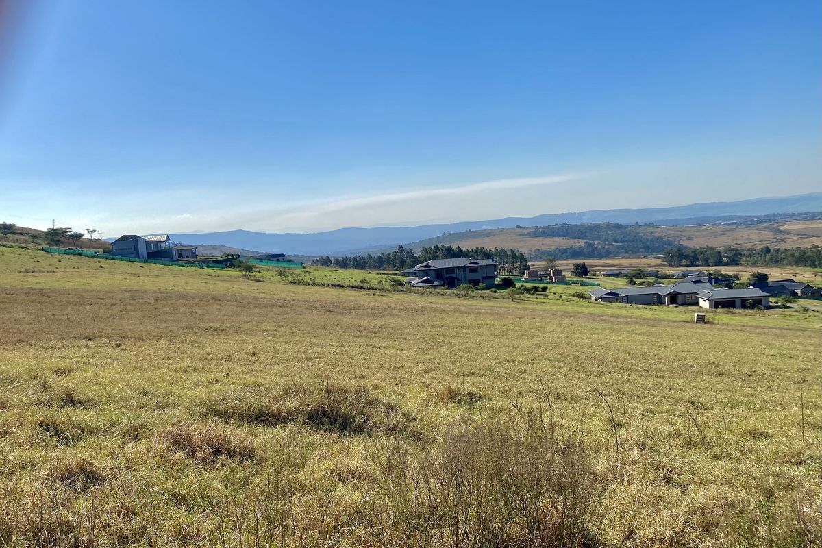 A wide-angle view of the vacant residential land, showcasing the surrounding landscape and neighboring properties under a clear blue sky.