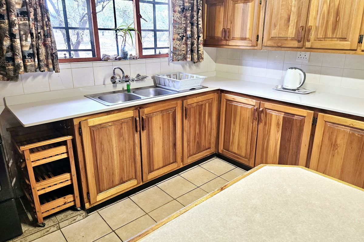 A functional kitchen featuring traditional wooden cabinetry, a double basin sink, tiled backsplash, and tiled flooring with ample counter space.