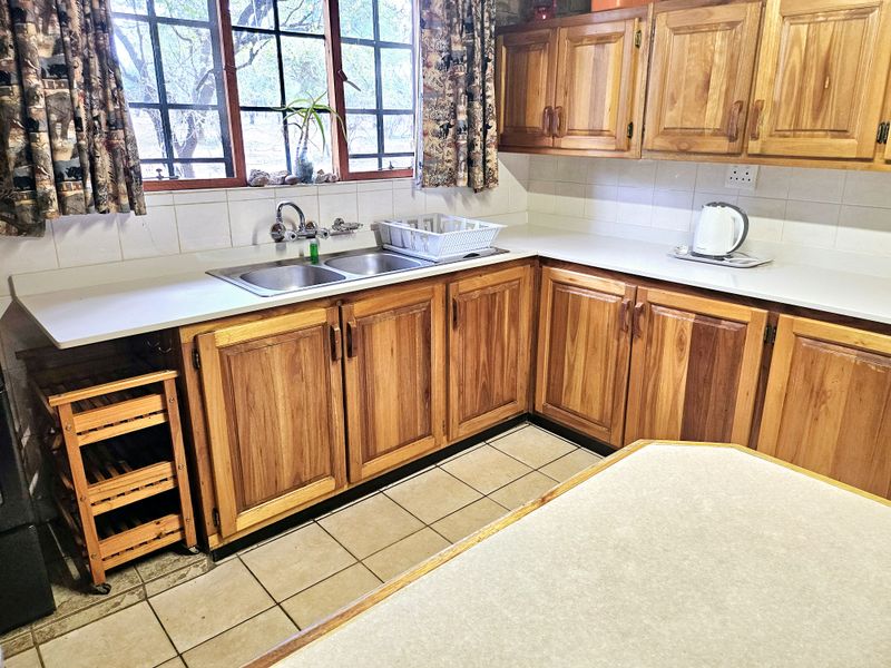 A functional kitchen featuring traditional wooden cabinetry, a double basin sink, tiled backsplash, and tiled flooring with ample counter space.