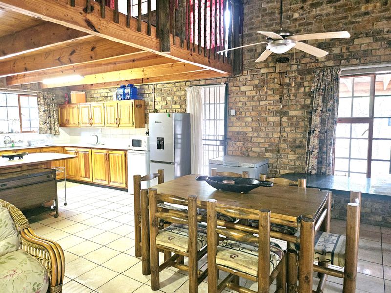Open-plan kitchen and dining area featuring exposed brick walls, timber ceiling beams, and a mezzanine level, offering a rustic aesthetic with functional layout.