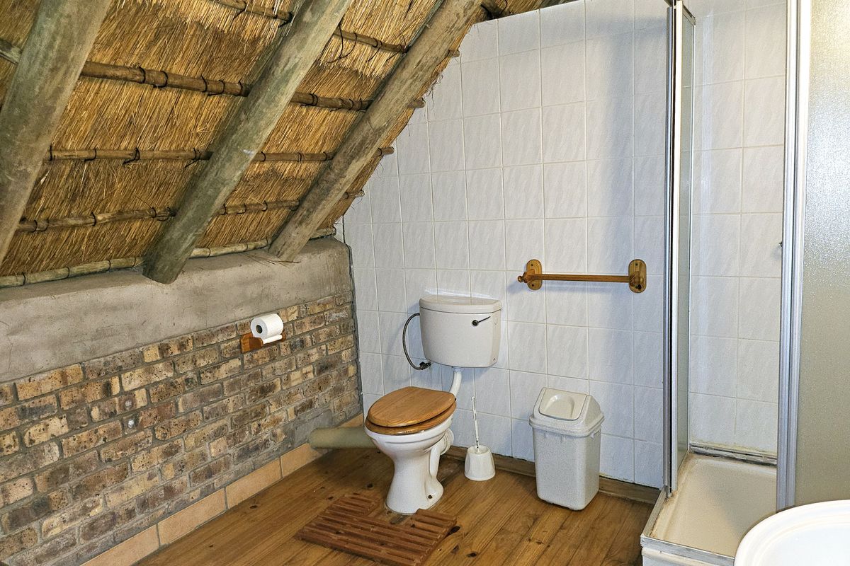 Bathroom featuring a unique thatched roof with exposed rafters, brick wall accents, tiled shower enclosure, and timber flooring.