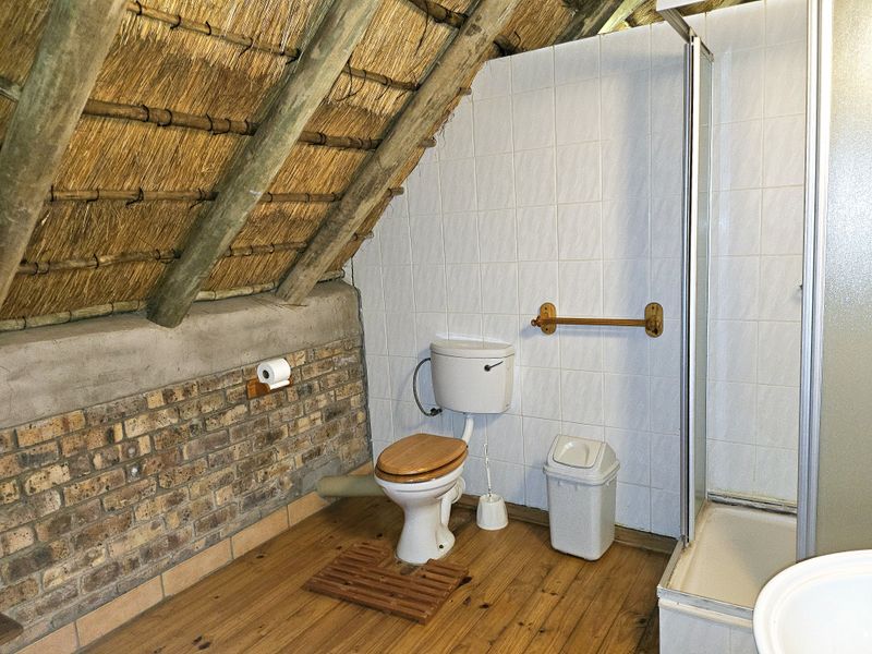 Bathroom featuring a unique thatched roof with exposed rafters, brick wall accents, tiled shower enclosure, and timber flooring.