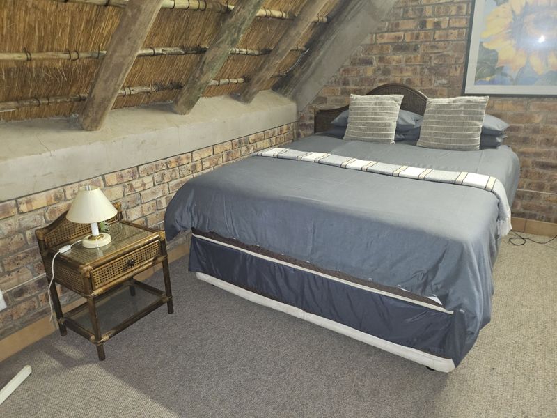 A cozy bedroom featuring rustic face brick walls and an exposed thatch roof with timber rafters, creating a unique, character-filled living space.