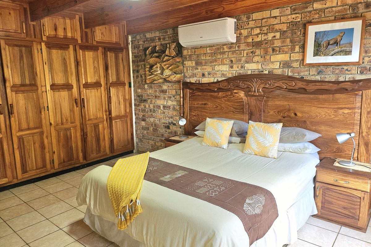 A rustic bedroom featuring exposed brick walls, timber ceiling beams, tiled flooring, and extensive built-in wooden cabinetry.