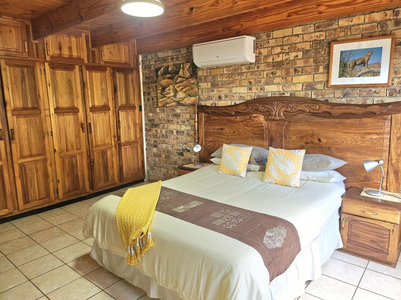 A rustic bedroom featuring exposed brick walls, timber ceiling beams, tiled flooring, and extensive built-in wooden cabinetry.