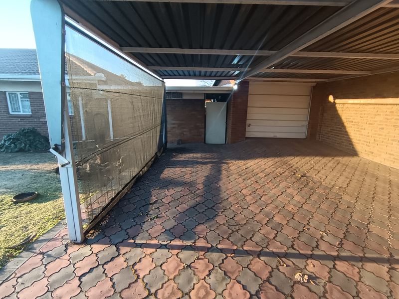 A covered carport area featuring paved flooring, brick walling, and a secure garage door entrance.