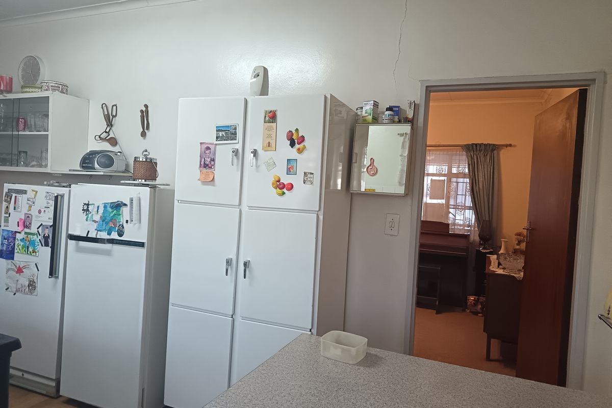 A dated kitchen area featuring built-in cabinetry and a laminate countertop, with a visible structural crack above the doorway leading to an adjacent room.
