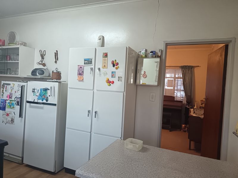 A dated kitchen area featuring built-in cabinetry and a laminate countertop, with a visible structural crack above the doorway leading to an adjacent room.