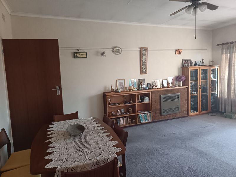 A living room featuring a built-in brick fireplace, ceiling fan, and carpeted flooring, offering a functional space with potential for modernization.