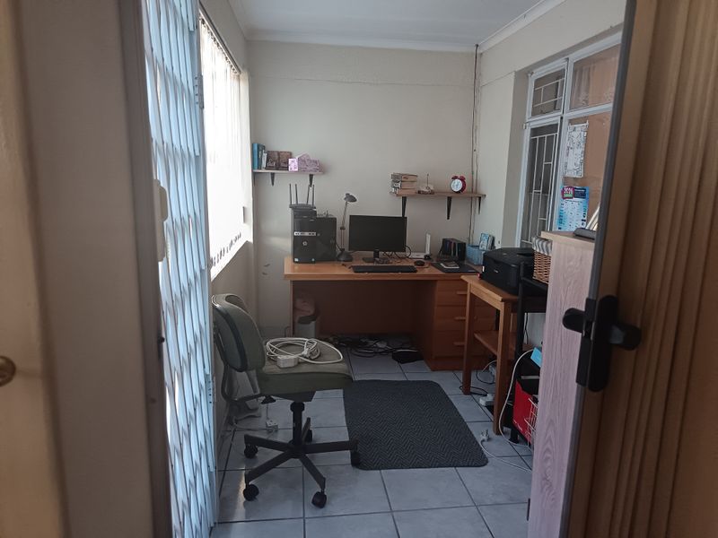 A functional home office space featuring tiled flooring, security gates, and window blinds, providing a practical area for work or study.