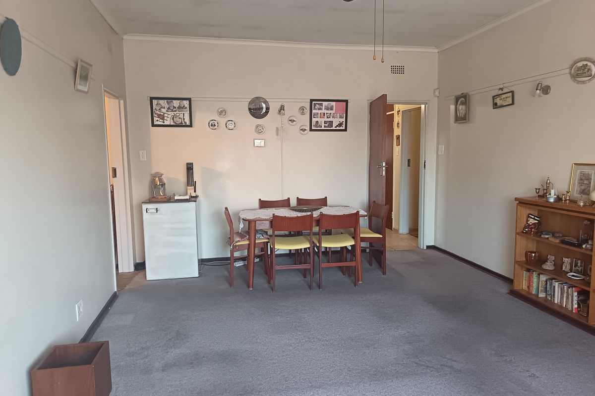 A spacious living area featuring carpeted flooring and a ceiling fan, offering a neutral canvas for potential updates and modernization.