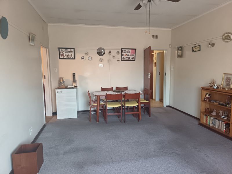 A spacious living area featuring carpeted flooring and a ceiling fan, offering a neutral canvas for potential updates and modernization.