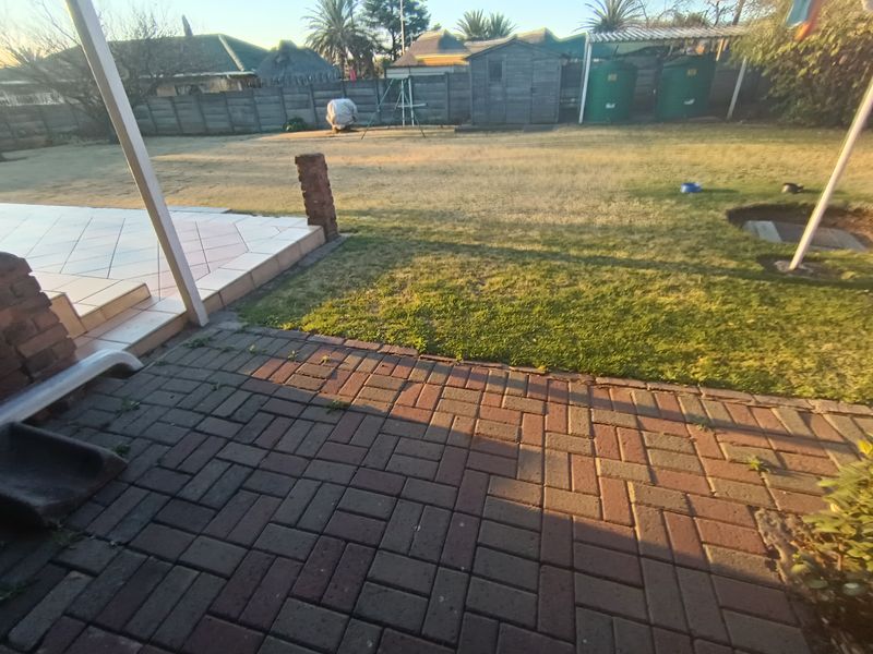 A spacious rear garden featuring a tiled patio, brick paved area, perimeter walling, and practical outdoor storage solutions.