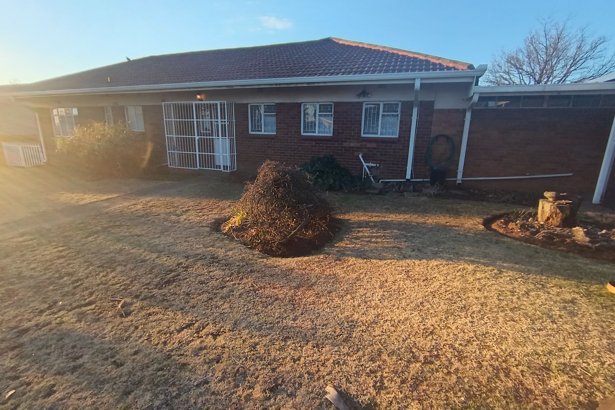Rear view of a single-story brick house featuring a tiled roof, security bars on windows, and a garden area.