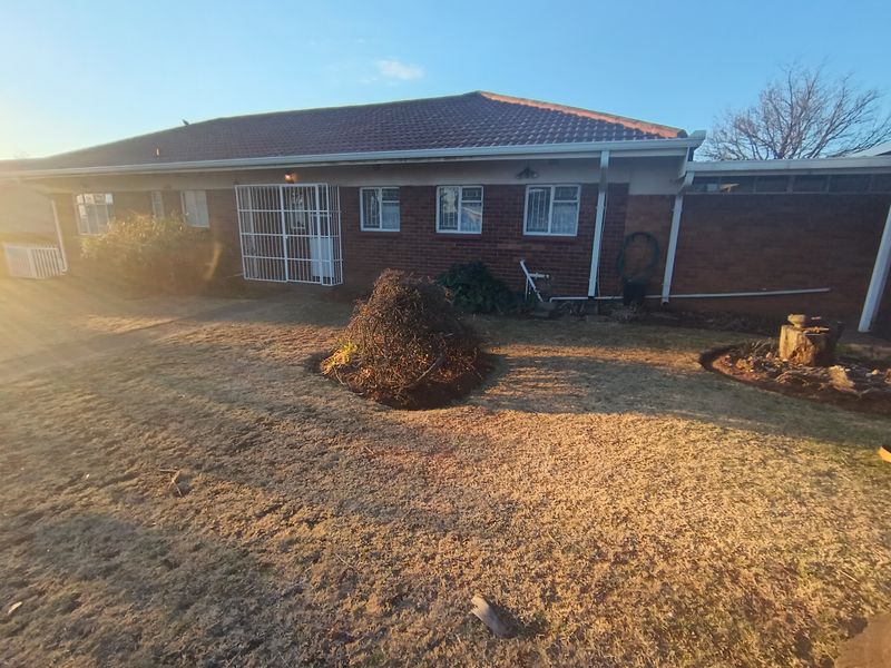 Rear view of a single-story brick house featuring a tiled roof, security bars on windows, and a garden area.