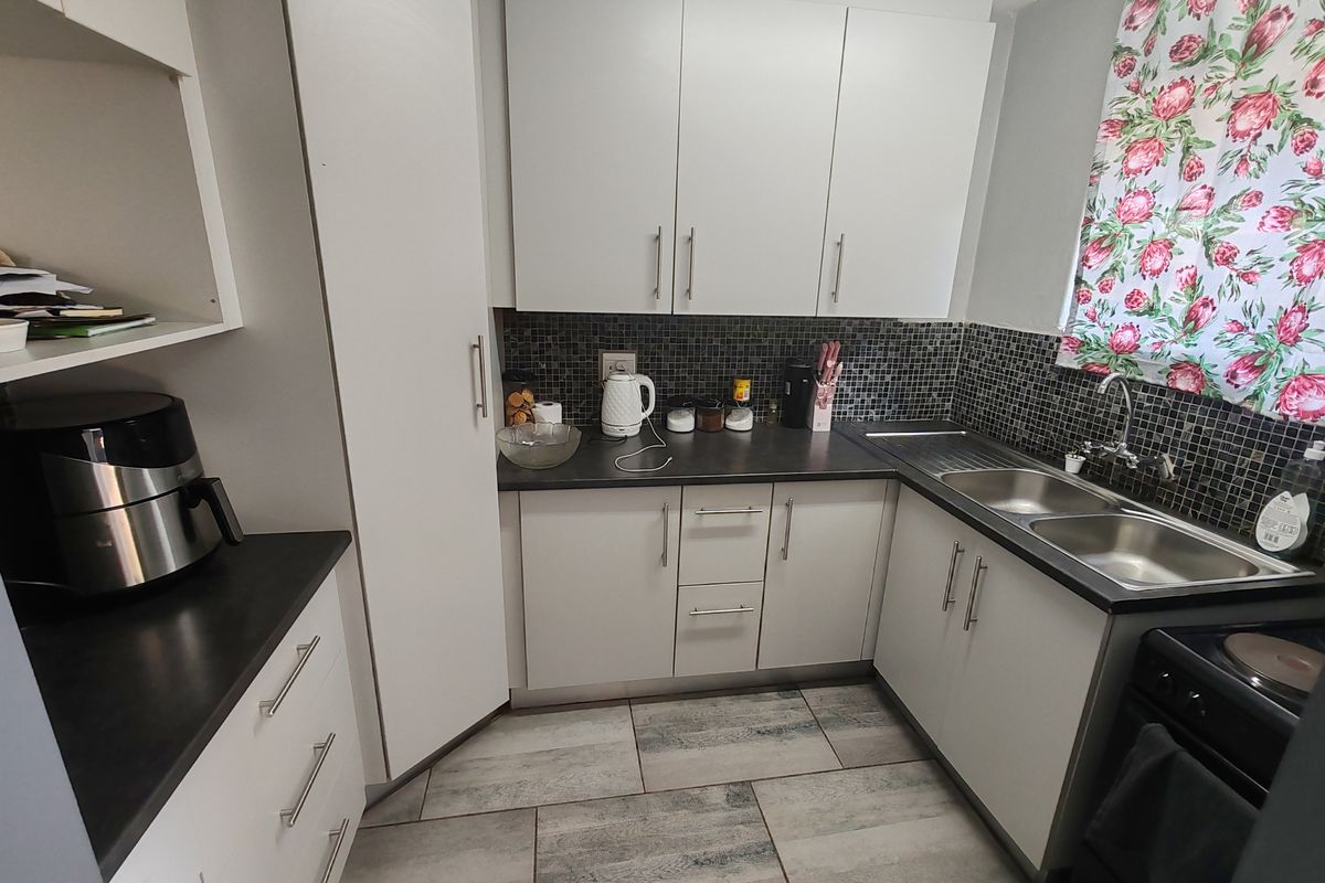 A functional kitchen featuring white cabinetry, dark laminate countertops, a mosaic tile backsplash, and a double basin stainless steel sink.