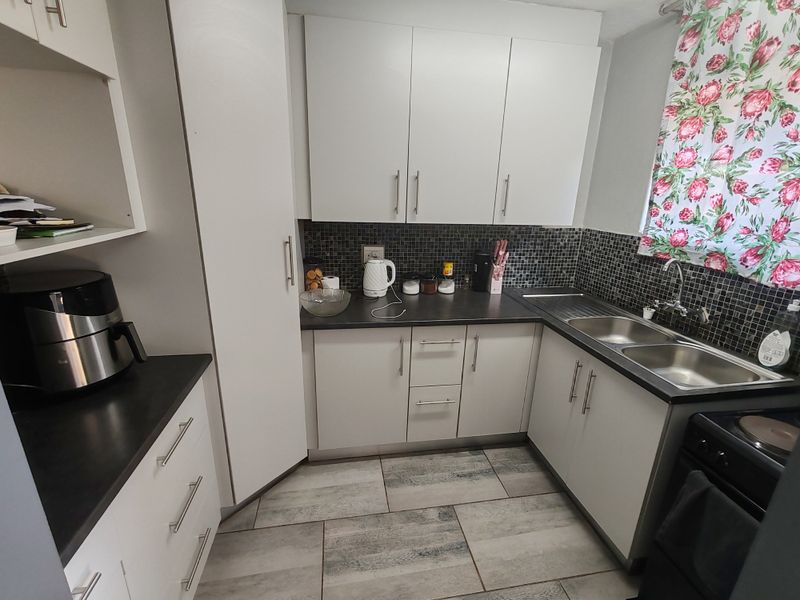 A functional kitchen featuring white cabinetry, dark laminate countertops, a mosaic tile backsplash, and a double basin stainless steel sink.