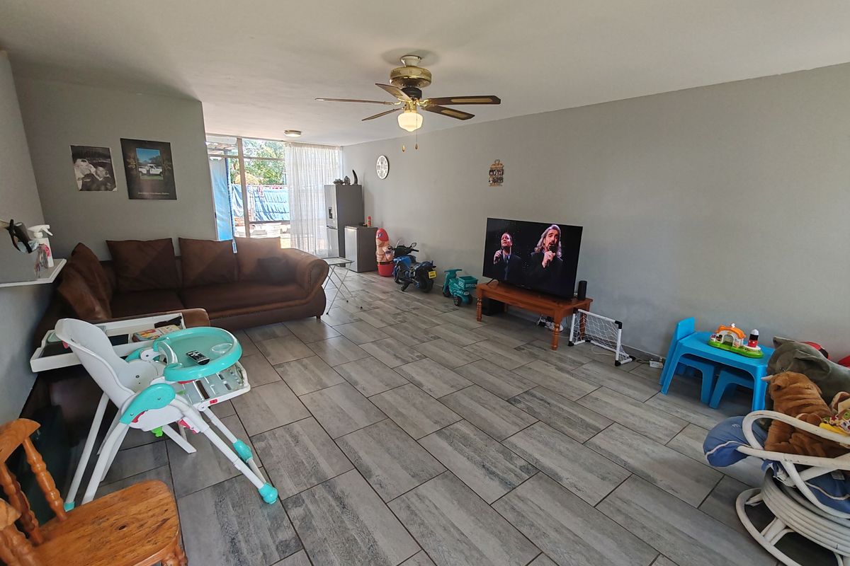 Spacious living room featuring modern grey tiled flooring, a ceiling fan, and large sliding glass doors providing access to the outdoor area.