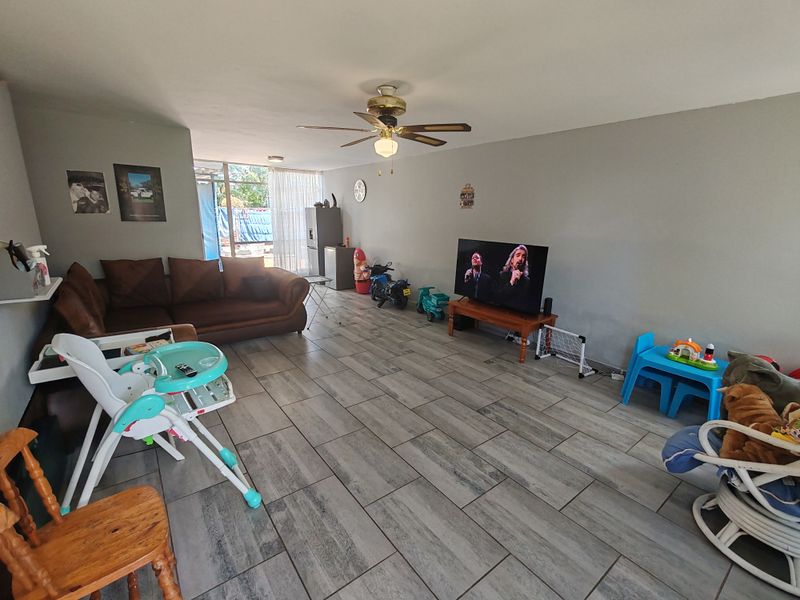 Spacious living room featuring modern grey tiled flooring, a ceiling fan, and large sliding glass doors providing access to the outdoor area.