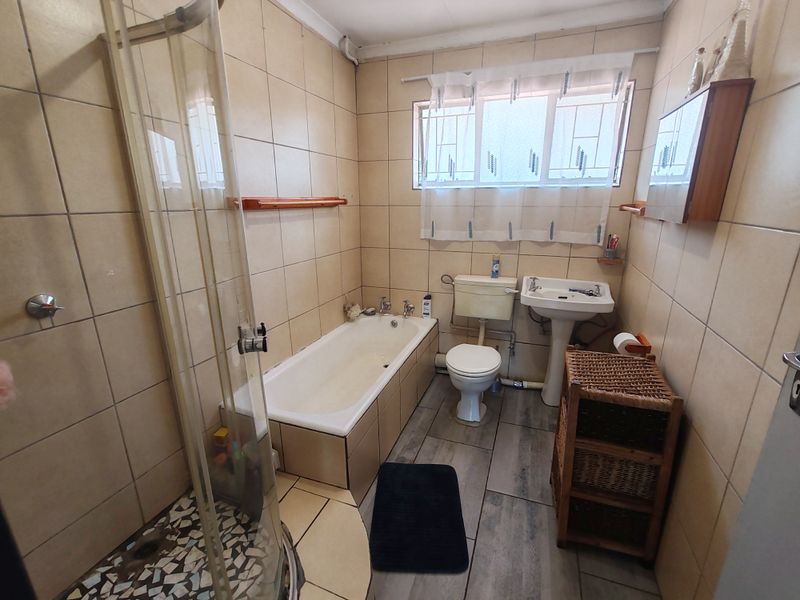 A functional bathroom featuring a shower enclosure, bathtub, pedestal basin, and toilet, finished with neutral wall tiles and wood-look floor tiles.