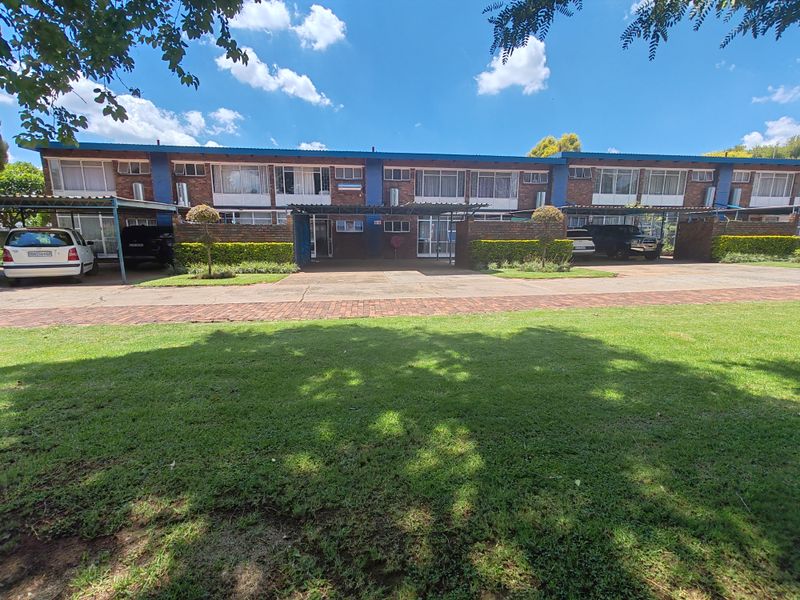 Front elevation of a townhouse complex featuring brick facade, paved driveway access, and established lawn area.