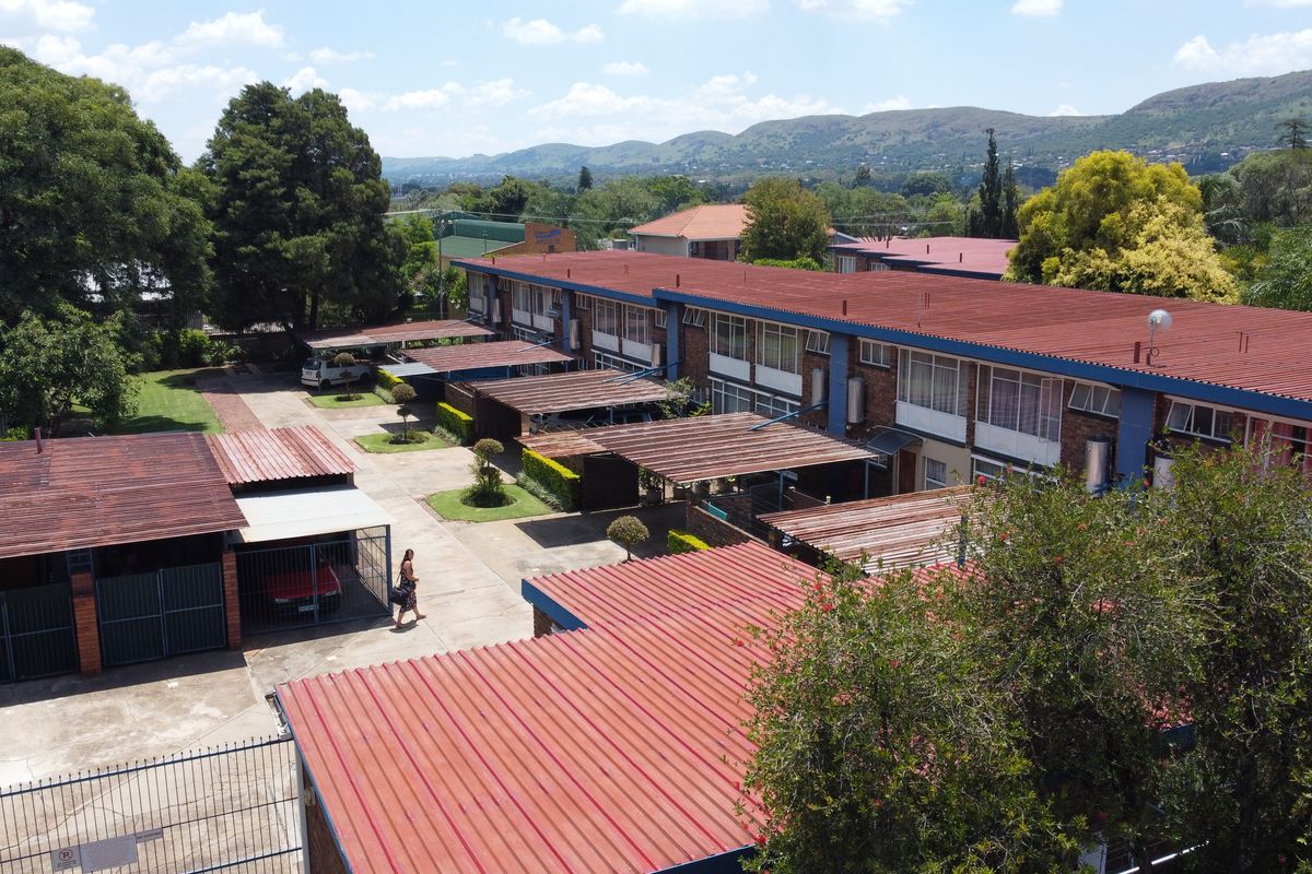 Aerial view of a townhouse complex featuring multiple units with corrugated metal roofs, dedicated carport parking, and paved driveway access.