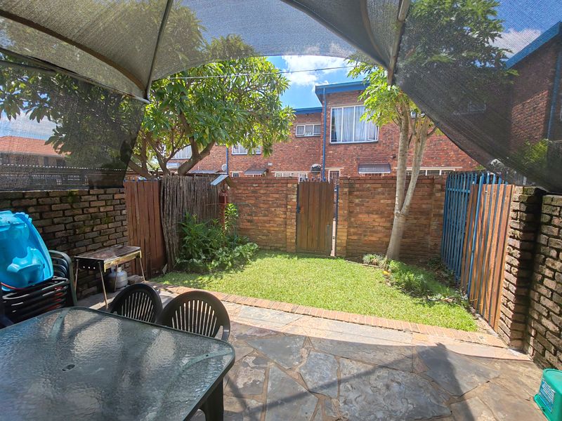Private rear courtyard featuring a stone-paved patio, brick boundary walls, and a shade sail, offering a functional outdoor entertainment space.