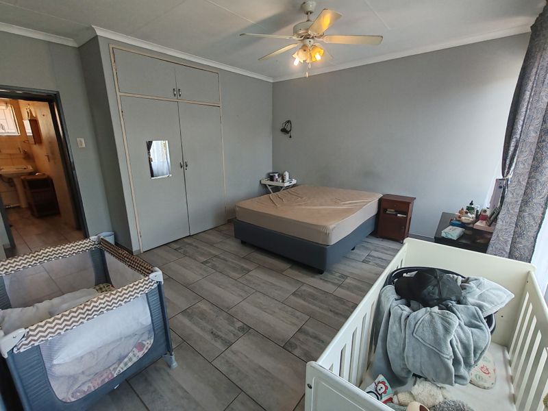 Spacious bedroom featuring tiled flooring, built-in cupboards, and a ceiling fan, with an adjoining en-suite bathroom.