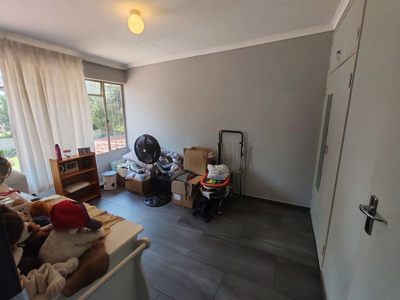 A bedroom featuring built-in cupboards, tiled flooring, and natural light from a window.