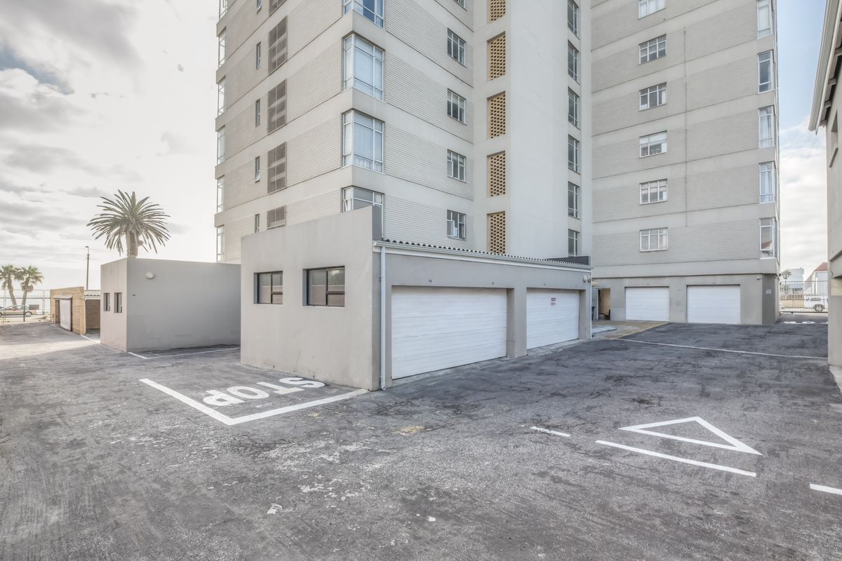 Rear exterior view of the apartment complex featuring a paved parking area and multiple garage units with a multi-story building facade.