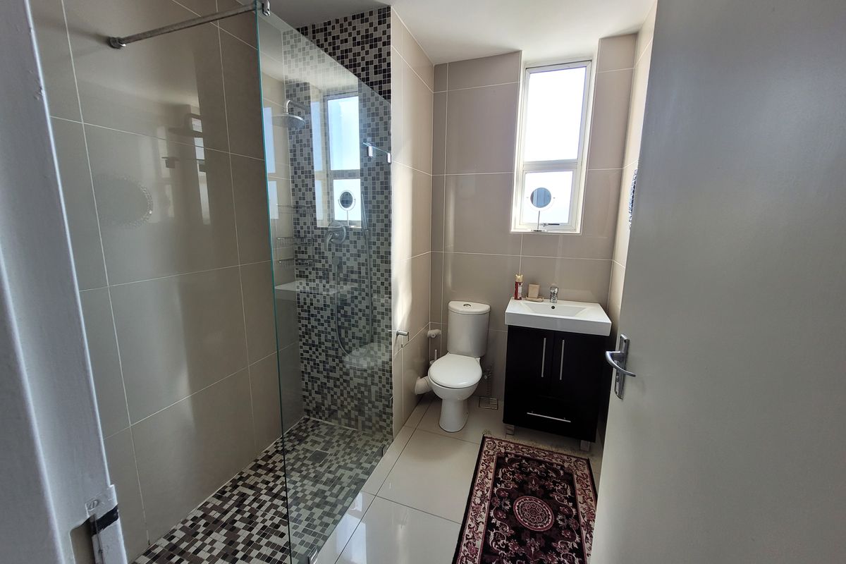 Modern bathroom featuring a glass-enclosed shower with mosaic tile accents, a vanity basin, and a toilet, finished with neutral wall and floor tiles.