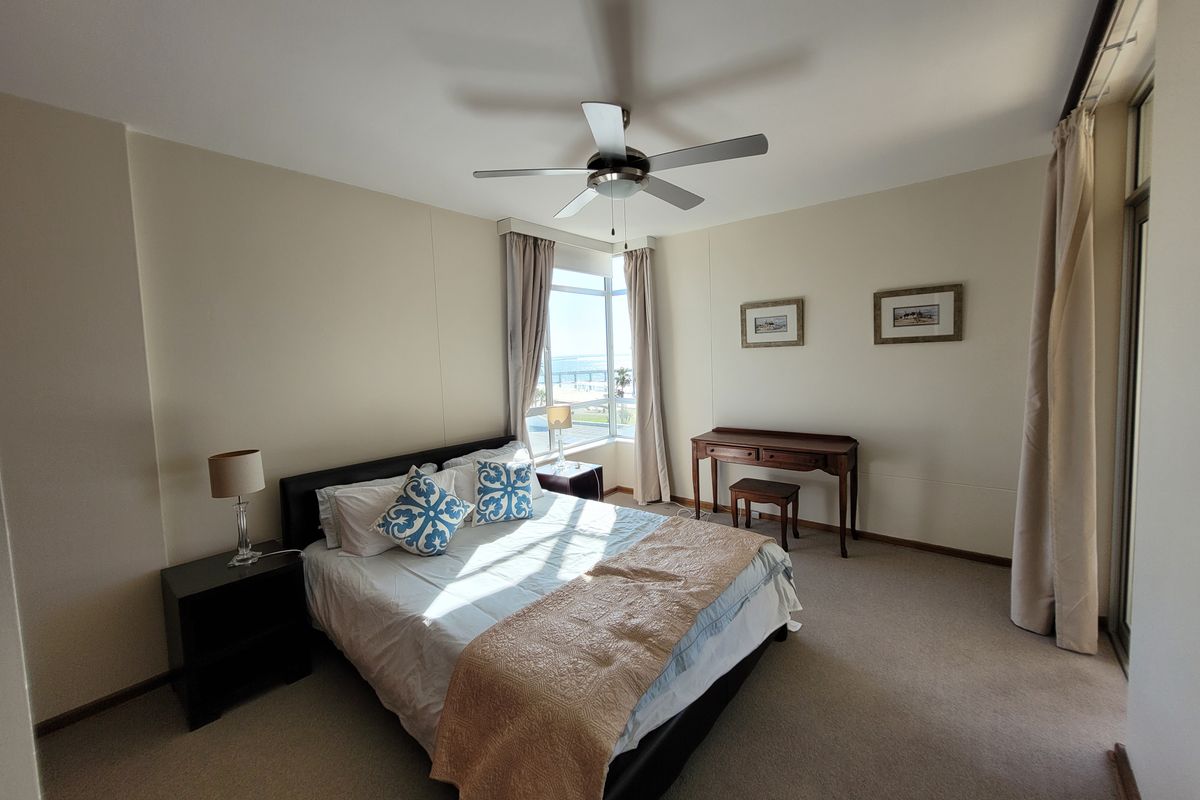 A spacious bedroom featuring neutral walls, carpeted flooring, a ceiling fan, and large windows with natural light and views.