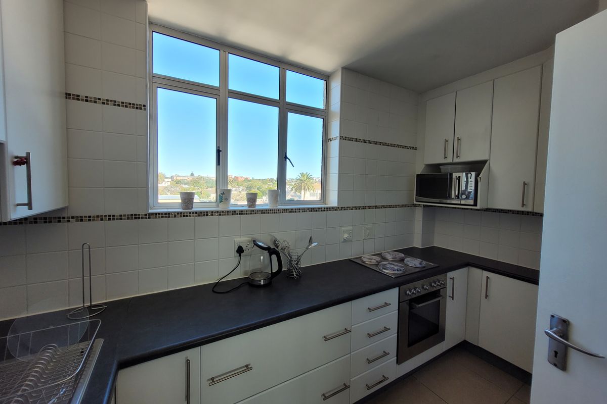 A functional kitchen featuring white cabinetry, dark laminate countertops, built-in oven and hob, and a large window providing natural light.
