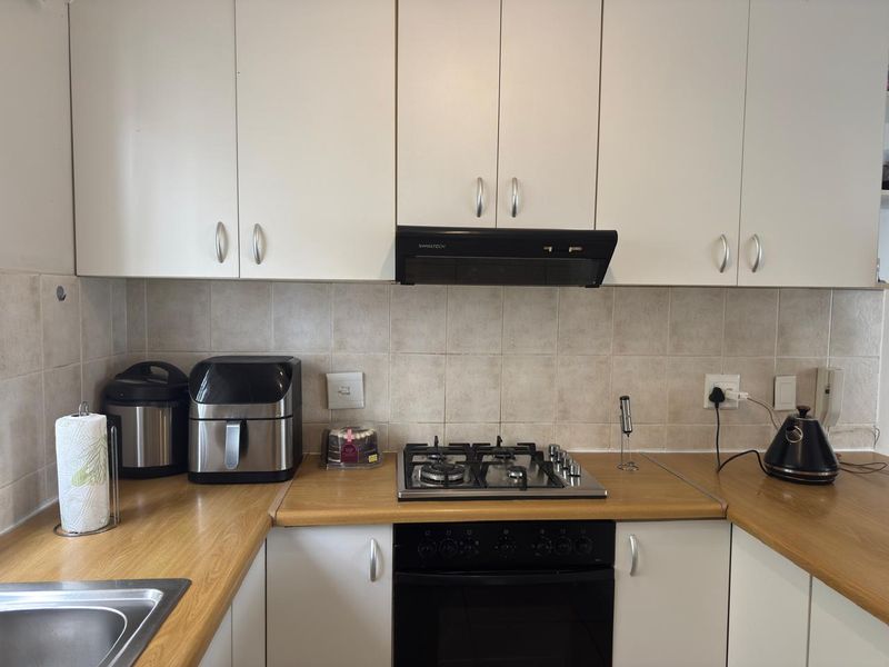 A functional kitchen featuring white cabinetry, laminate countertops, a gas hob, built-in oven, and a tiled backsplash.