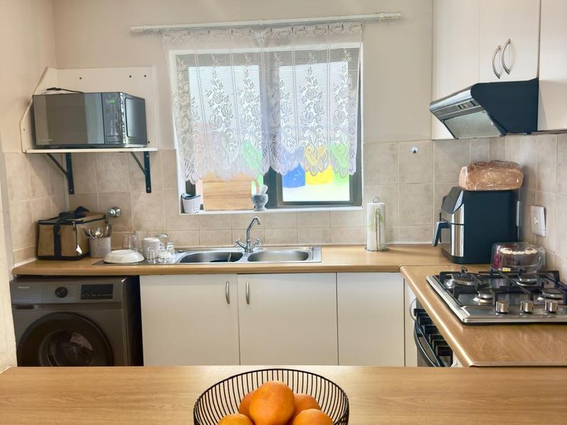 Functional kitchen featuring white cabinetry, wood-look laminate countertops, a gas hob with extractor, and a built-in oven with an integrated washing machine.